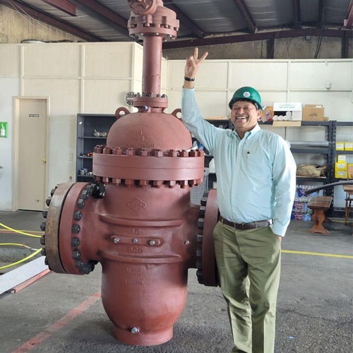 Man in a green hard hat standing next to a large red-brown industrial valve in a workshop
